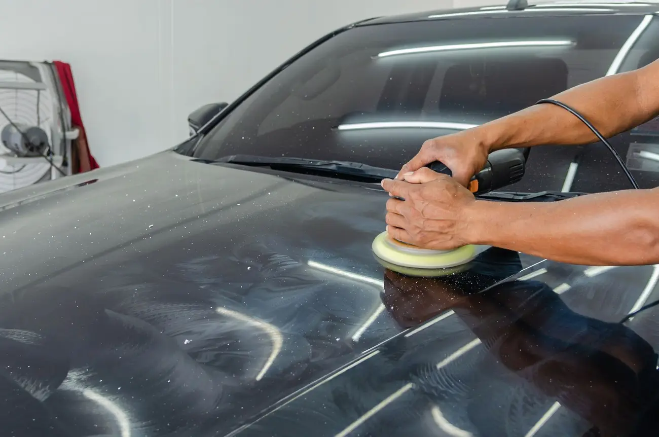 Machine polisher working across a dark car bonnet